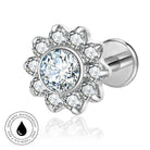 Silver-toned flower-shaped stud earring with a large clear round center stone and surrounding clear petal stones, shown on a white background with a circular skin-safe waterproof badge.