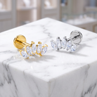 Two leaf-shaped stud earrings displayed on a white marble block. One earring is gold-toned with marquise-cut clear stones, and the other is silver-toned with marquise-cut clear stones.