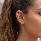 Close-up of a woman's ear showing two earrings: a small gold hoop earring and a silver starburst-shaped cartilage piercing.