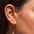 Close-up of a person's ear showcasing a gold huggie hoop earring and a silver ear cuff with clear marquise-cut stones.