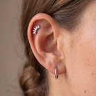 A close-up of a person's ear showcasing a silver leaf cluster ear cuff and a simple silver hoop earring against a neutral beige background.
