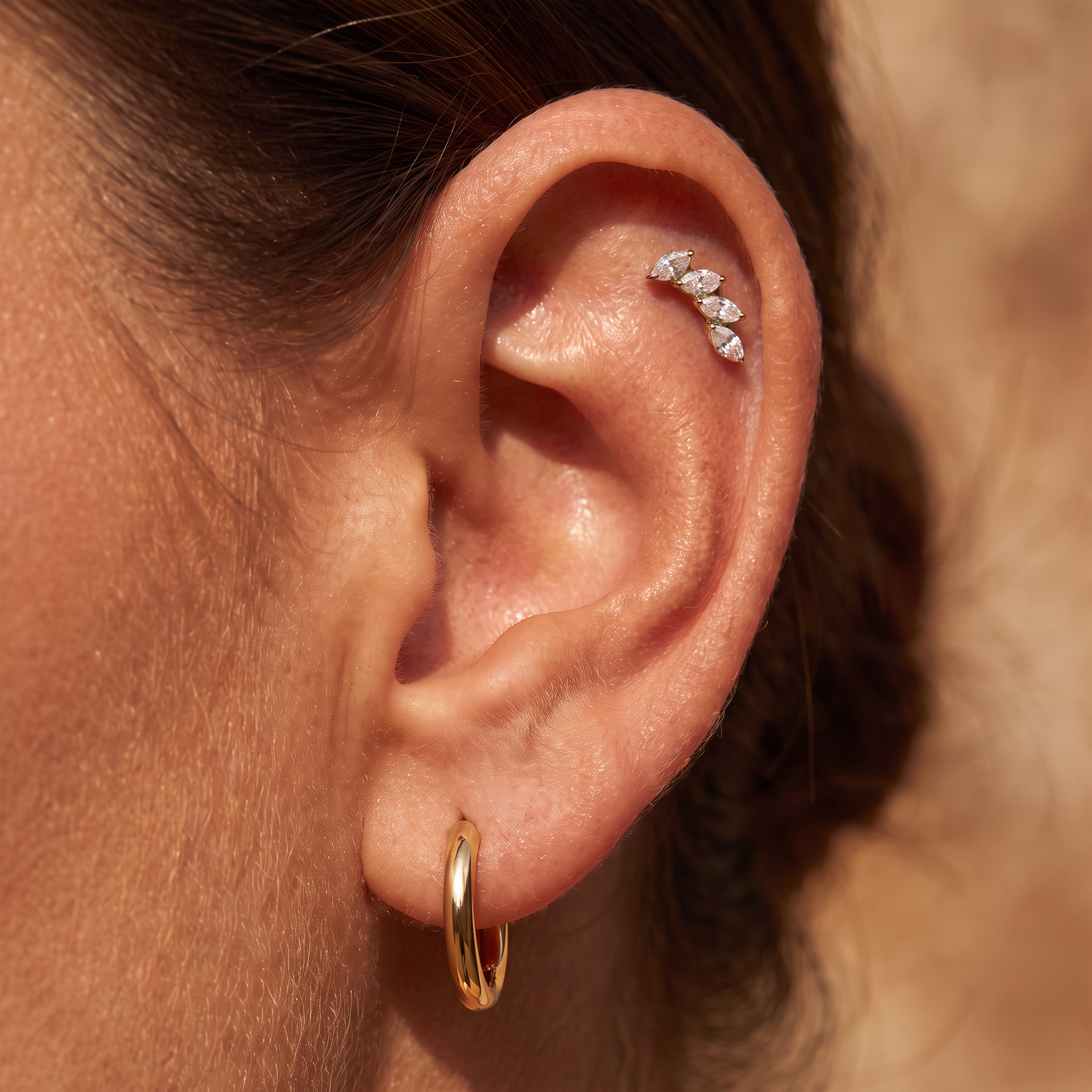 Close-up of a person's ear showcasing a gold hoop earring in the lobe and a silver leaf cluster stud in the cartilage.