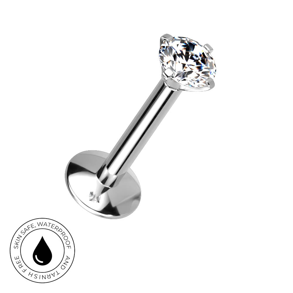 A silver-toned labret piercing barbell with a clear faceted gemstone, shown on a plain white background with a circular 'Skin Safe Waterproof' badge in the lower-left corner.