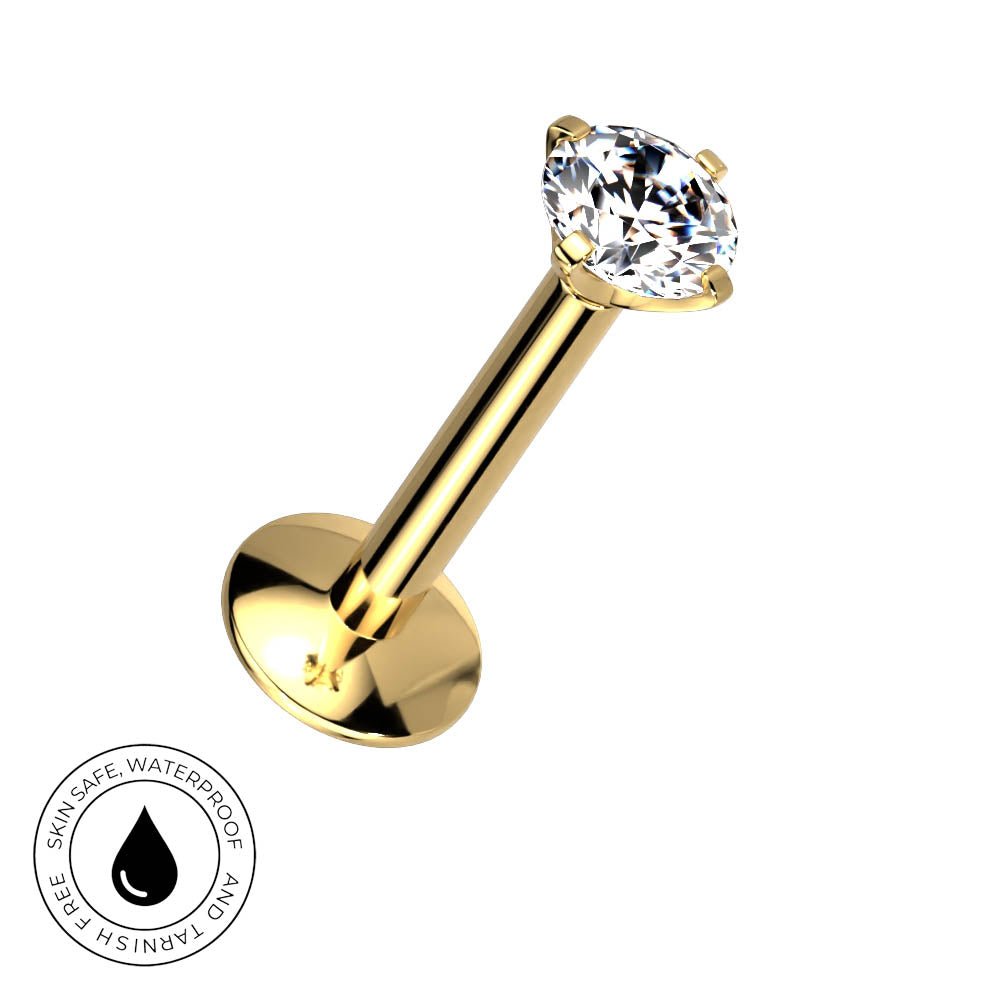 A gold-plated labret piercing barbell with a clear faceted gemstone in a four-prong setting, shown on a plain white background with a circular 'Skin Safe Waterproof' certification badge in the bottom-left corner.