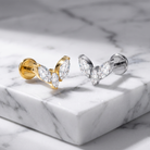 Two butterfly-shaped stud earrings with marquise-cut clear stones, one in yellow gold and one in silver, displayed on a white marble block.