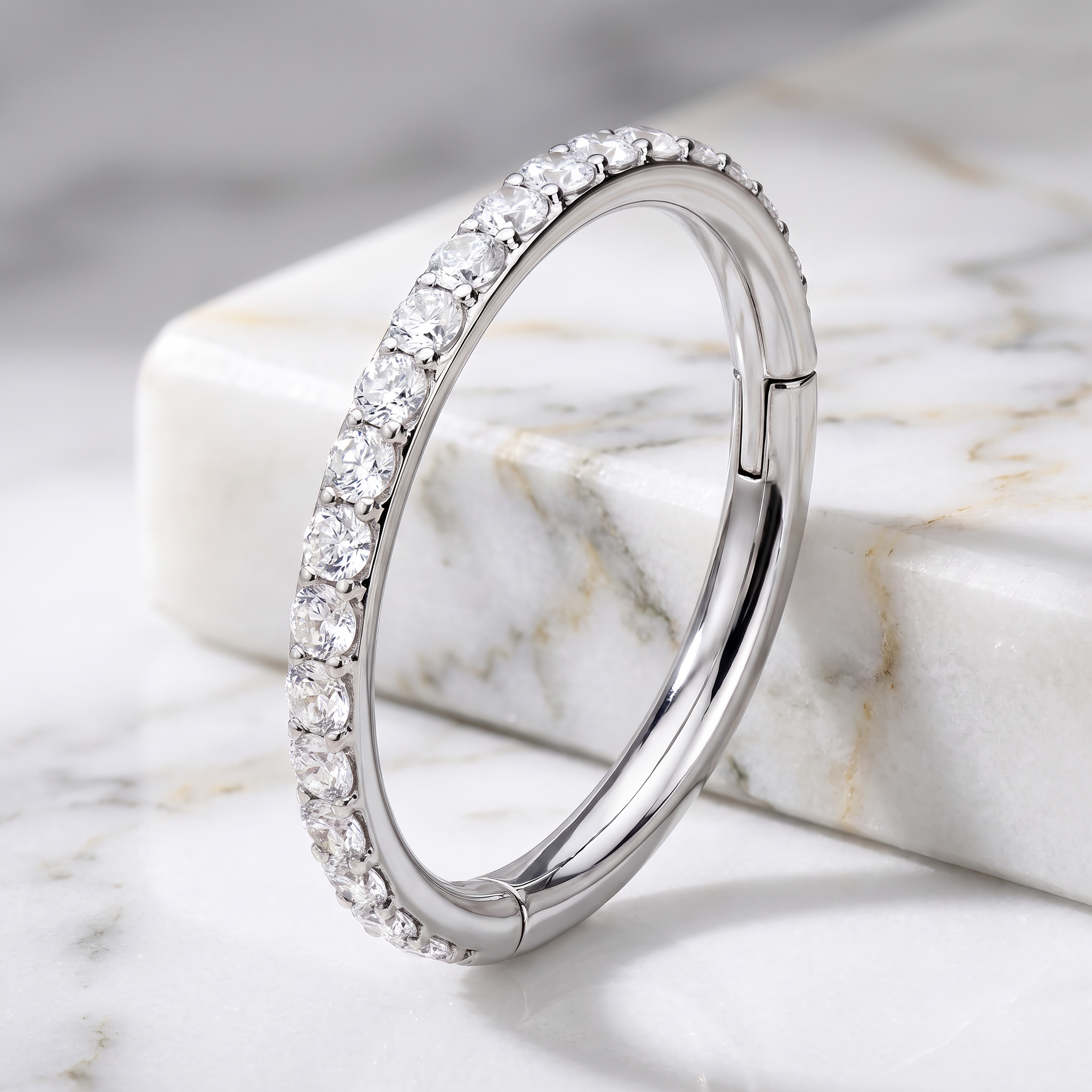 A polished silver-toned huggie hoop ring set with a full row of clear cubic zirconia stones, displayed on a white and gray marble block.