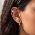 Close-up of a person's ear showing a small silver ear cuff stud with a flower-like design and a silver hoop earring.