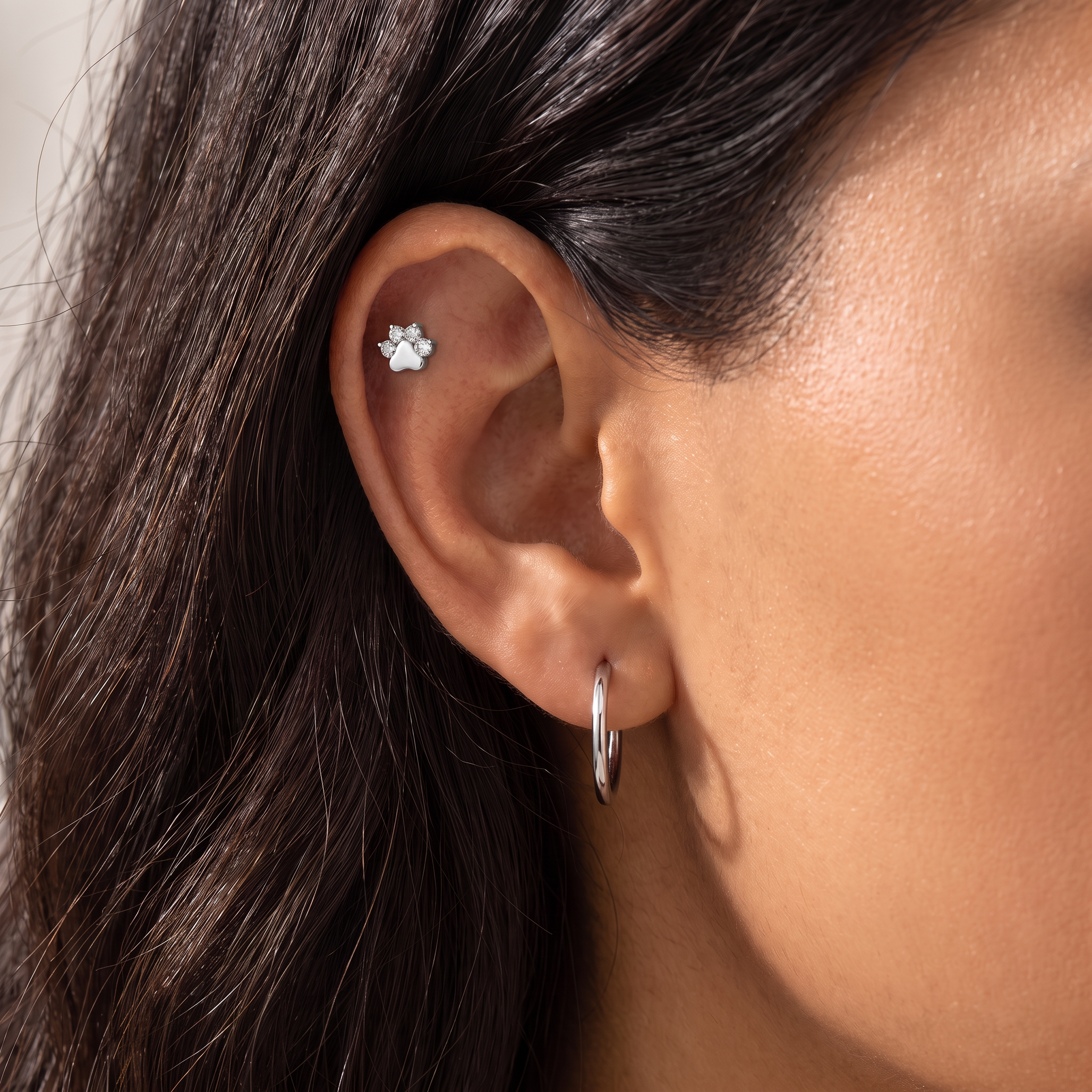 Close-up of a person's ear showing a small silver ear cuff stud with a flower-like design and a silver hoop earring.