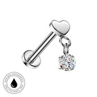 A silver-toned barbell-style body jewelry piece with a heart-shaped end and a dangling clear round gemstone charm, shown on a white background with a small skin-safe waterproof badge in the lower left.