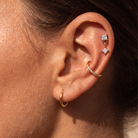 Close-up of a person's ear showcasing multiple gold and silver stud earrings, including a small gold hoop, a gold ear cuff with clear stones, and a double-drop silver stud with a clear star-shaped gem.