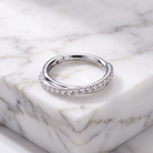 A silver-toned huggie ring with a row of clear pavé stones on one side, resting on a white marble block.