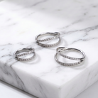 Three silver hoop earrings with pavé-set clear stones, arranged on a white marble slab.