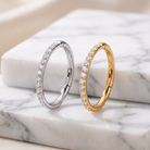Two slim hoop-style rings with pavé-set clear stones, one in silver-toned metal and one in yellow gold-toned metal, displayed on a white marble surface.