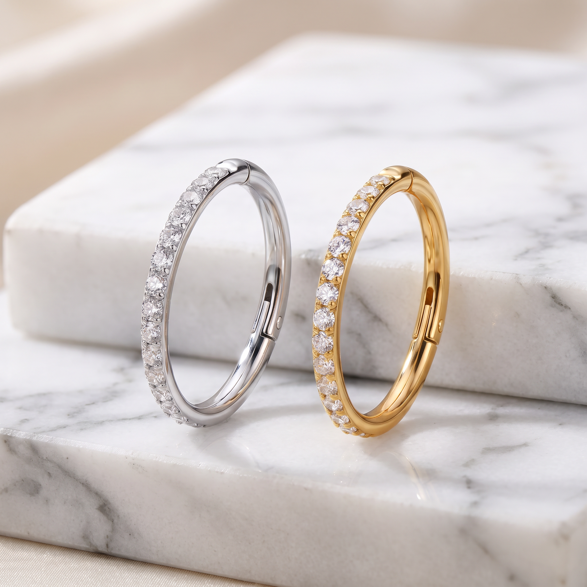 Two slim hoop-style rings with pavé-set clear stones, one in silver-toned metal and one in yellow gold-toned metal, displayed on a white marble surface.