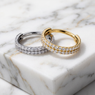 Two diamond hoop rings, one in yellow gold and one in silver, displayed on a white marble block with natural gray veining.