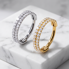 Two hoop earrings with double rows of clear pavé stones, one in silver-tone metal and one in yellow gold-tone metal, displayed on a white marble block.
