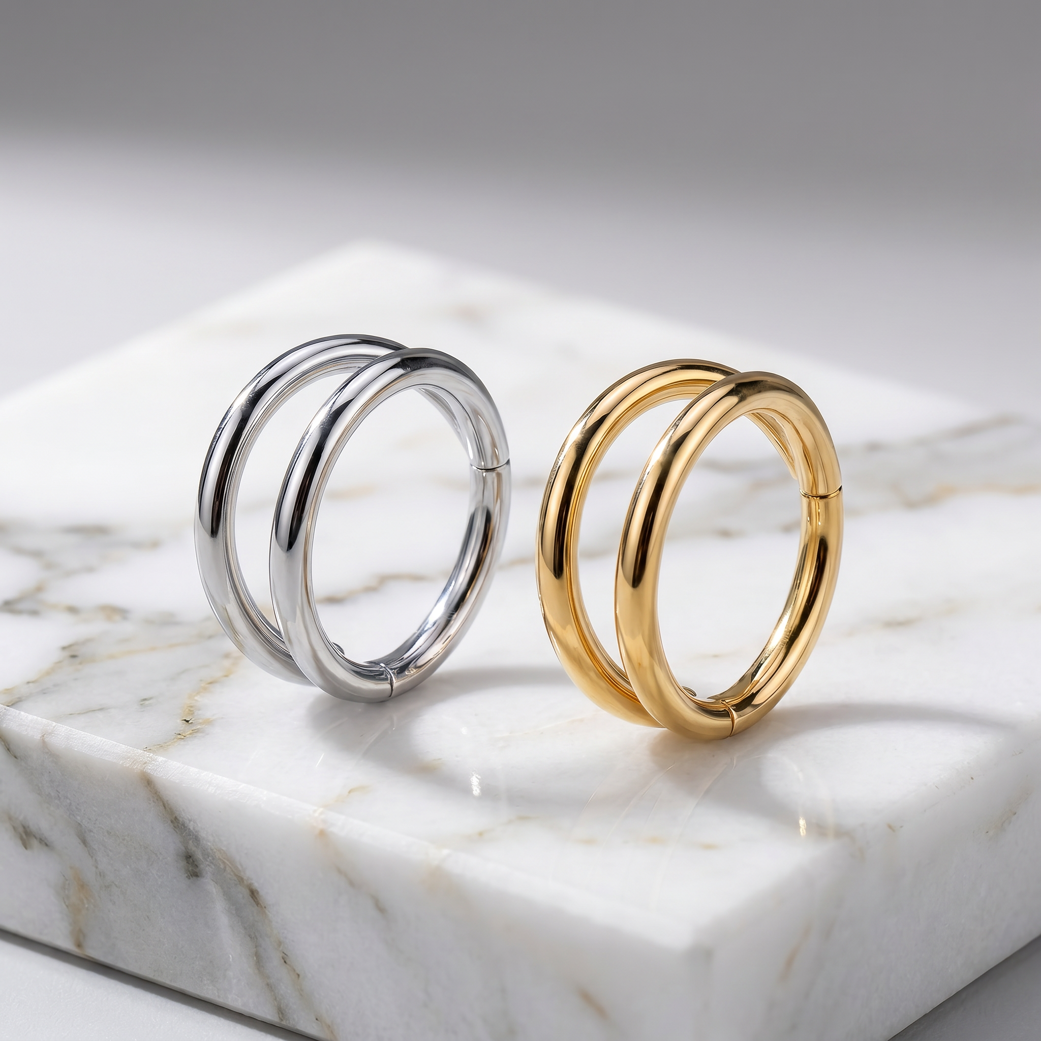 Two double-hoop earrings, one polished silver-tone and one polished yellow gold-tone, displayed side-by-side on a white marble block.