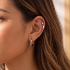 A close-up of a woman's ear showcasing a silver ear cuff with a small crescent moon and a classic silver hoop earring.
