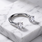 A silver circular barbells with two square-cut clear gemstones, displayed on a white marble block.