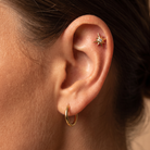 Close-up of a person's ear showcasing a gold hoop earring in the lobe and a gold starburst ear cuff on the helix.