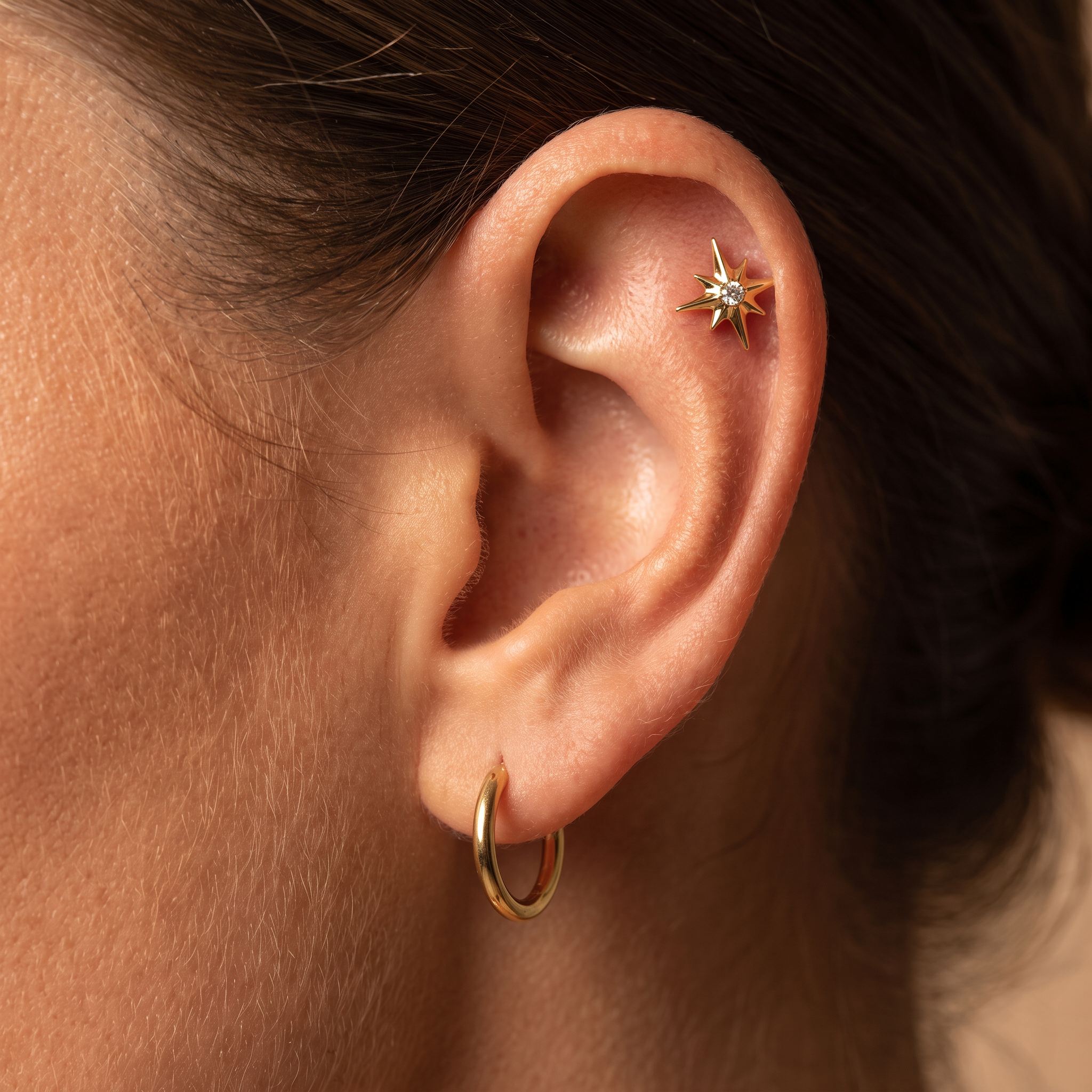 Close-up of a person's ear showcasing a gold hoop earring in the lobe and a gold starburst ear cuff on the helix.