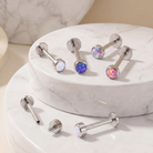 Six silver-toned labret piercing studs with colorful opal-like round faceted tops, displayed on white marble round pedestals.