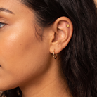 Close-up of a person's ear wearing a small gold hoop earring and a gold star-shaped cartilage piercing, with dark hair and warm skin tones.
