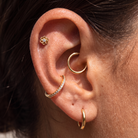 Close-up of a person's ear showcasing multiple gold ear piercings, including a small flower stud, a curved hoop, a diamond-accented huggie, and a lower hoop.