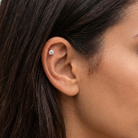 A close-up of a person's ear wearing a small round stud earring with a silver-toned metal setting and clear gemstone.