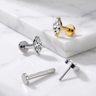 Four stud earrings with marquise-cut clear gemstones and post backings, shown on a white marble surface and a white marble block. Two earrings are silver-toned and two are gold-toned.