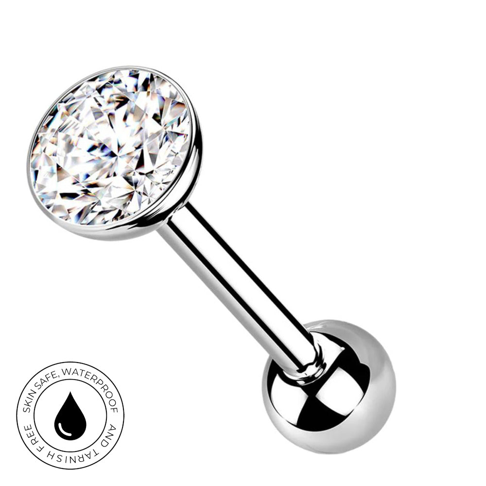 A silver-toned labret piercing barbell with a large round clear faceted gemstone on one end and a polished ball on the other, shown on a white background with a small circular skin-safe waterproof badge in the lower left.