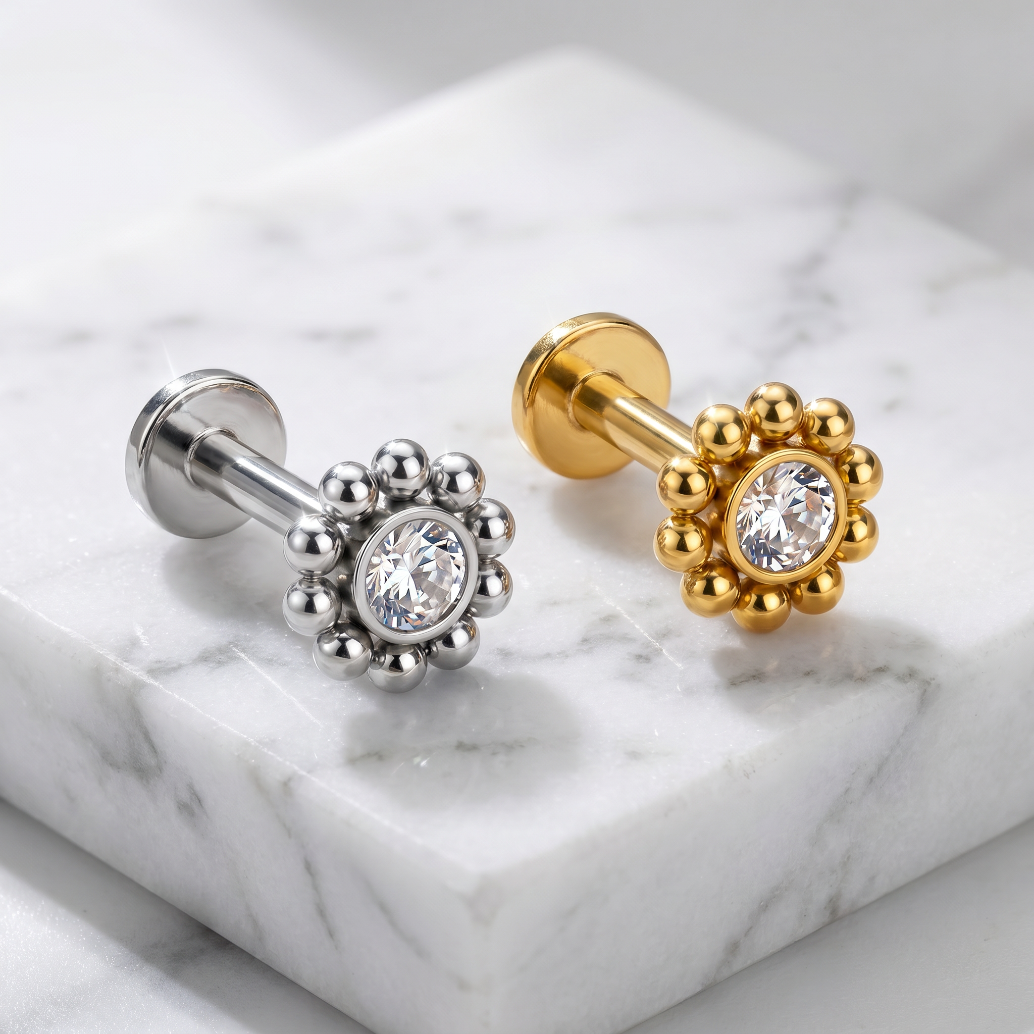 Two flower-shaped stud earrings displayed on a white marble block. One earring is silver-toned and the other is gold-toned, both featuring a central clear crystal surrounded by small metallic petals.
