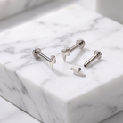 Four silver-toned lightning bolt stud earrings arranged on a white marble block with gray veining.