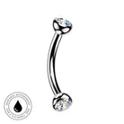 A curved barbell piercing jewelry piece with clear faceted gemstones on both ends, shown on a plain white background with a circular 'Skin Safe Waterproof' badge in the lower left corner.