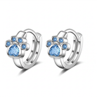 A pair of silver huggie hoop earrings featuring a paw print design with light blue heart-shaped and round gemstones, set against a plain white background.