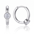 A pair of polished silver huggie hoop earrings, one shown from the front with a round clear gemstone in a halo setting and the other from the side showing the hinge and the gemstone setting, on a white background with a soft reflection.