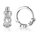 A pair of polished silver huggie hoop earrings with stacked heart charms, shown on a clean white background with soft reflections.