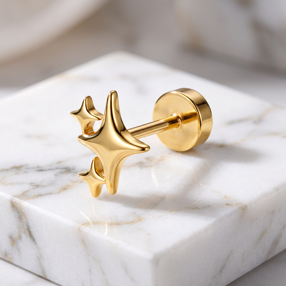 A gold star-shaped stud earring with a polished circular post and backing, displayed on a white marble block.