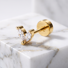 A gold post piercing stud with two marquise-cut clear gemstones, displayed on a white marble block.