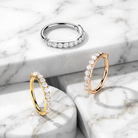 Three diamond hoop rings in silver, yellow gold, and rose gold, arranged on a white and gray marble pedestal background.