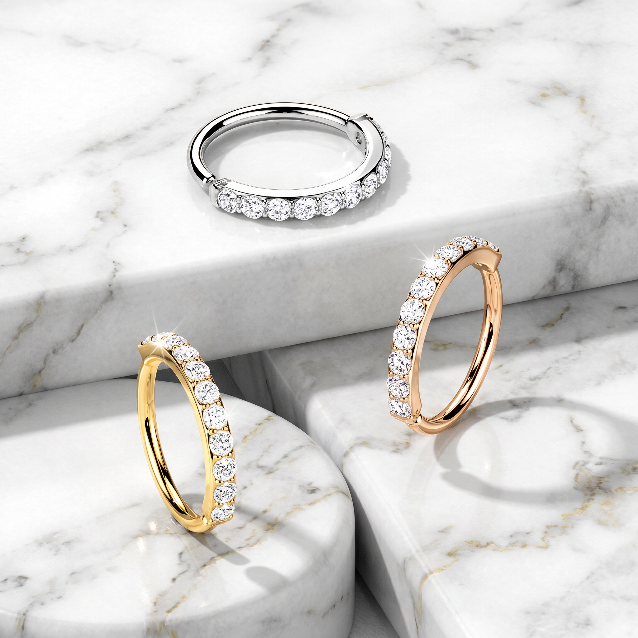 Three diamond hoop rings in silver, yellow gold, and rose gold, arranged on a white and gray marble pedestal background.