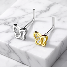 Two butterfly-shaped stud earrings on a white marble slab, one in silver and one in yellow gold, both with clear crystal accents.