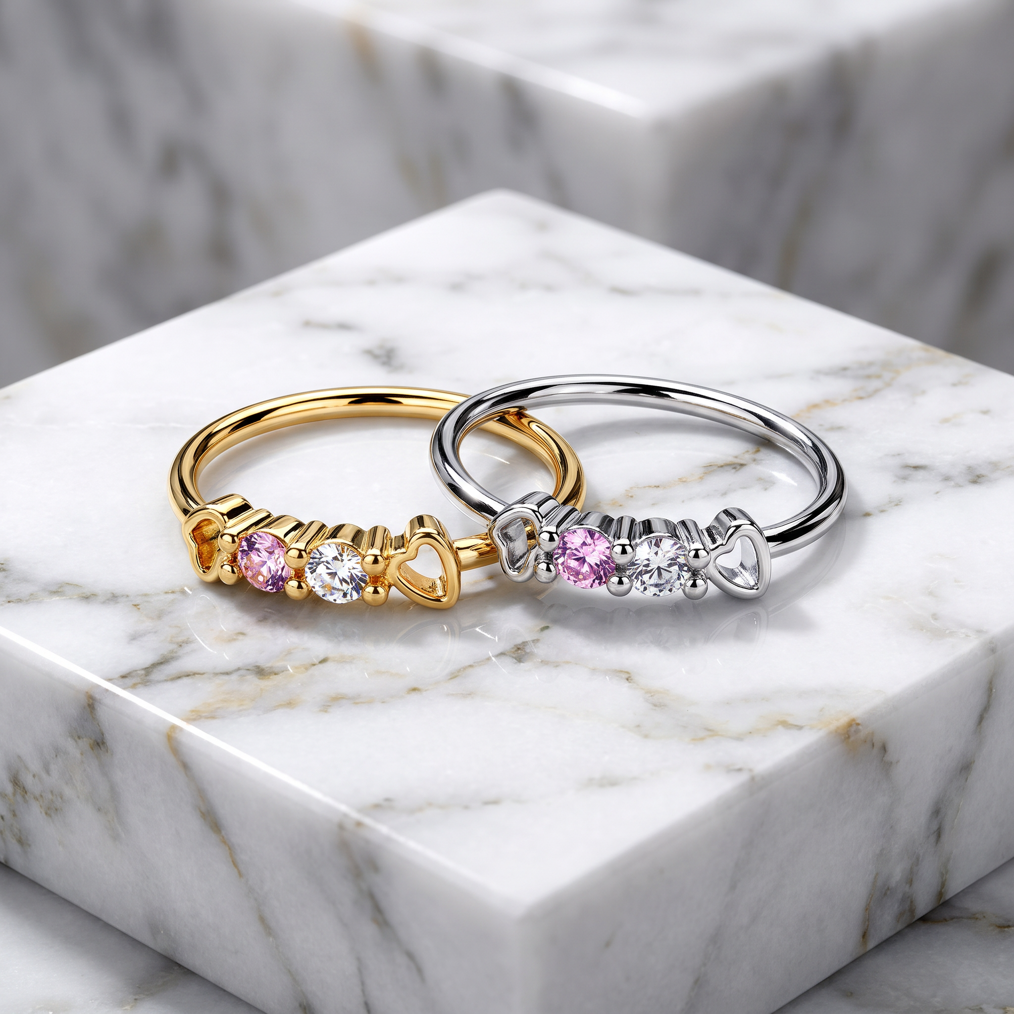 Two heart-shaped stretch rings displayed on a white marble pedestal. One ring is gold with pink and clear stones, and the other is silver with pink and clear stones.