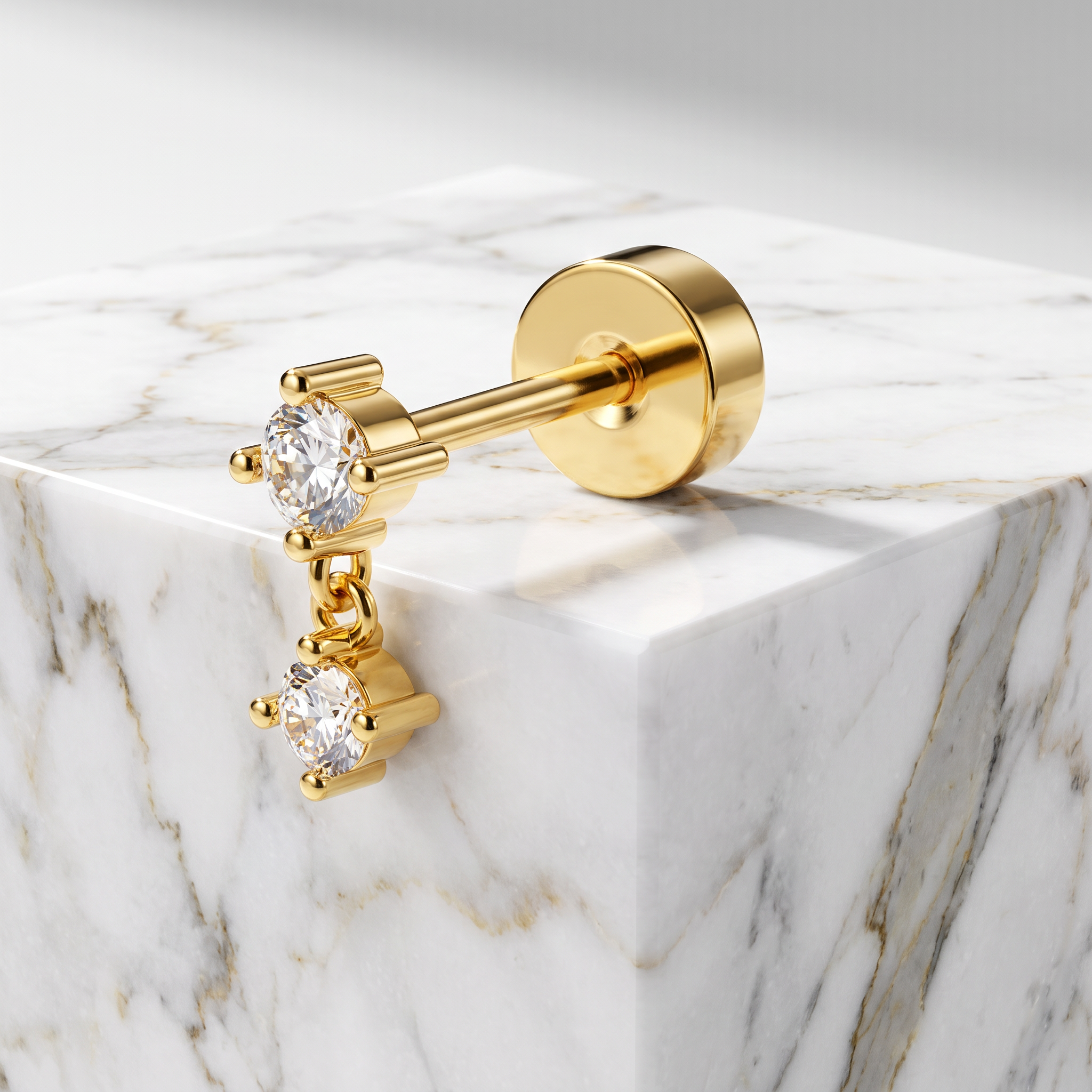 A pair of gold-plated stud earrings with clear gemstones, displayed on a white marble block against a light gray background.
