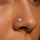 A close-up of a person's nose wearing a small heart-shaped silver stud earring.