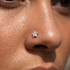 A close-up of a person's nose wearing a small star-shaped silver stud nose ring with a clear gemstone.