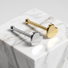Two heart-shaped labret studs, one in polished silver and one in polished gold, displayed on a white marble cube against a light gray background.