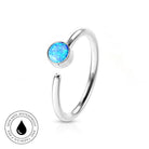 A silver-toned open ring with a round blue opal gemstone, shown on a white background with a small circular 'skin-safe waterproof' badge in the lower left corner.
