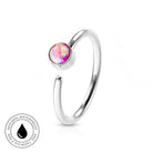 A silver-toned open bangle ring with a round bezel-set iridescent pink and purple stone, shown on a white background with a small circular 'skin-safe waterproof' badge in the lower left.