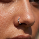 A close-up of a person's nose wearing a small twisted silver hoop nose ring.